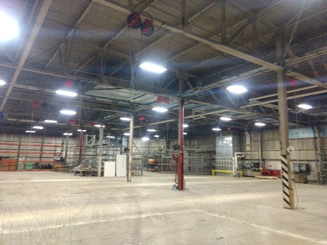 Interior of Building 7230 at Loring: a high-bay hall with exposed steel trusses, columns and overhead lighting over an open slab